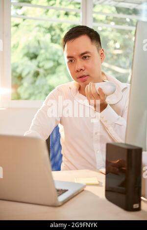 Serious young entrepreneur working at office desk and recording voice message for coworker Stock Photo