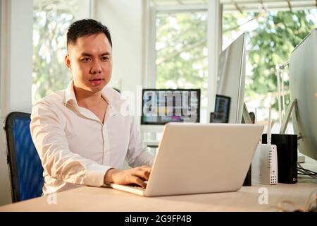 Serious frowning software developer working on laptop at his office desk Stock Photo
