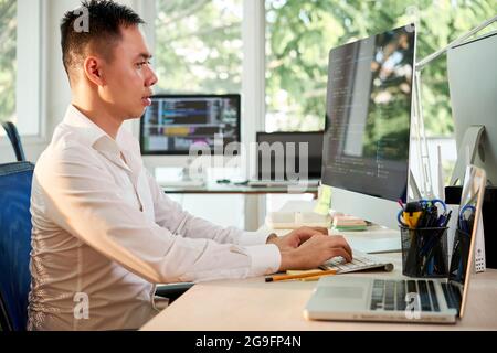 Side view of programmer sitting at office desk and coding on computer Stock Photo