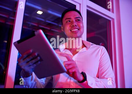 Happy young businessman working on tablet computer in dark office with led light Stock Photo