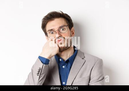 Bored funny office worker in glasses, pouting and holding breath, staring with popped eyes at camera, white background Stock Photo