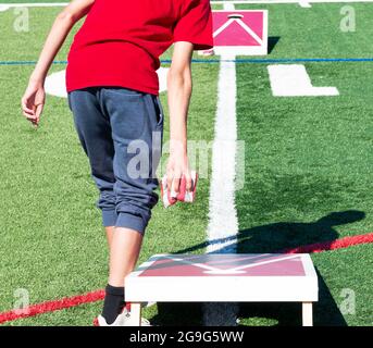 Rear view of a teenager throwing two bean hags while playing cornhole on a turf field. Stock Photo