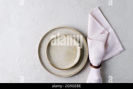 Beige ceramic plates and a pink napkin on a beige stone table. Top view, copy of space. Table setting, menu background, layout, recipe background, foo Stock Photo