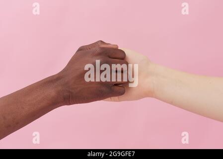 A handshake between an African American man and a Caucasian woman posing against a pink background, greeting each other, demonstrating international r Stock Photo