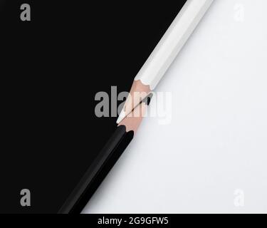 Macro shot of two black and white colored pencils with the tips touching on a matching background with opposite colors. Top down view flat lay Stock Photo