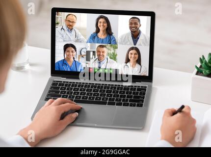 Female Doctor At Laptop Having Group Video Call With Team Of Therapists And Colleagues Communicating Online And Taking Notes Sitting At Workplace Indo Stock Photo