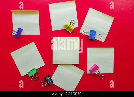 Blank yellow sticky notes and paper clip clips on a red background, business work concept. Yellow commemorative stickers on the red wall. Layout. Stock Photo