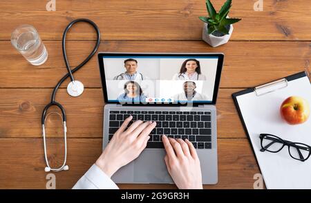 Above View Of Female Doctor Using Laptop Video Calling Diverse Colleagues Sitting At Workplace Indoor. Cropped Shot Of Medical Video Conference. Team Stock Photo