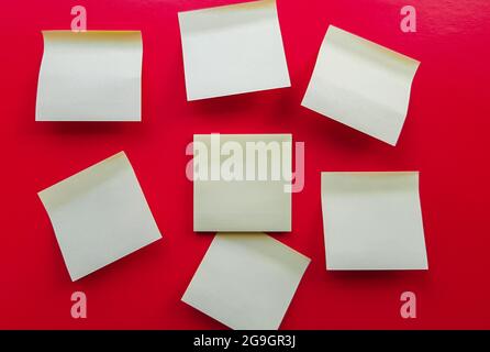 Blank yellow sticky notes on a red background, business work concept. Yellow commemorative stickers on the red wall. Layout. Stock Photo