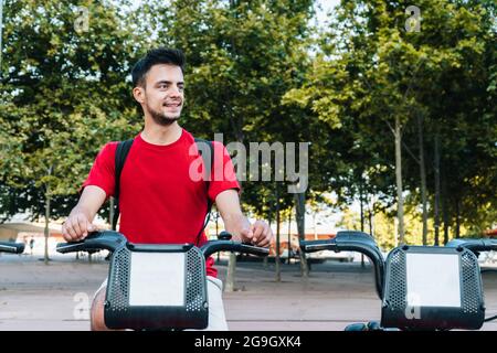 Young caucasian man smiling while sitting on a rented bicycle Stock Photo