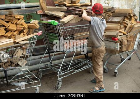 The child carries firewood. Firewood baskets. The boy collects fuel for heating. A child in an industrial area. Stock Photo