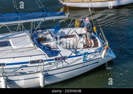 man helming steering driving a large racing yacht in the cockpit in the summer entering a marina. Stock Photo
