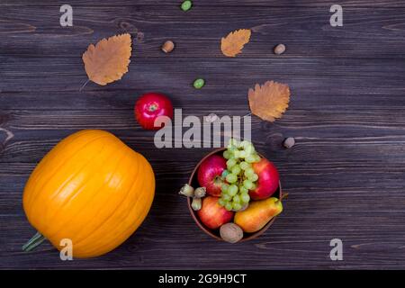 Orange pumpkins with apples and pears in a basket with grapes, nuts and leaves on a brown wooden table. View from above Stock Photo