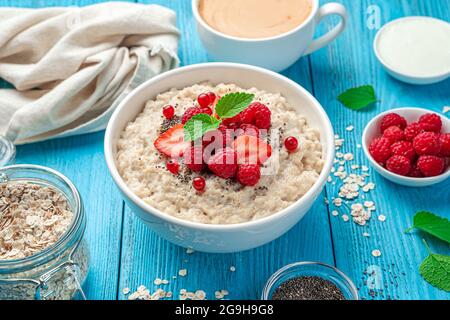 Oatmeal porridge with fresh berries and chia seeds on a blue background. Side view, close-up. Stock Photo