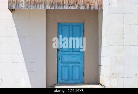 Older blue door in a white wall. The wall is made of light stone blocks. Stock Photo