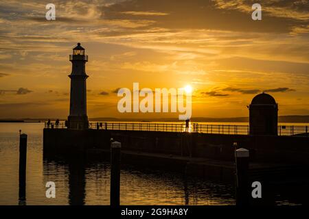 People silhouetted on pier at Newhaven harbour and lighthouse in a colourful orange sky at sunset, Edinburgh, Scotland, UK Stock Photo