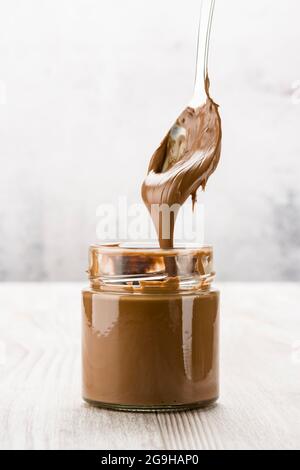 Chocolate cream in glass jar with dripping spoon, on wooden table Stock Photo