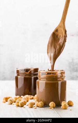 Chocolate cream in glass jar with hazelnuts and dripping spoon, on wooden table Stock Photo