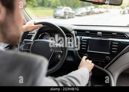Man using gps navigation system in car for travel on new road in city. Millennial attractive european man in suit holds hands on steering wheel, going Stock Photo