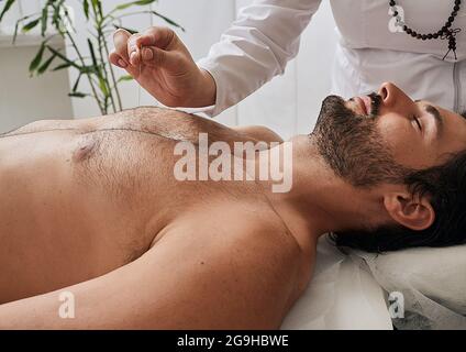 Acupuncturist inserts acupuncture needles at special points on man's body meridians. Acupuncture needles in reflexologist hand, close-up Stock Photo