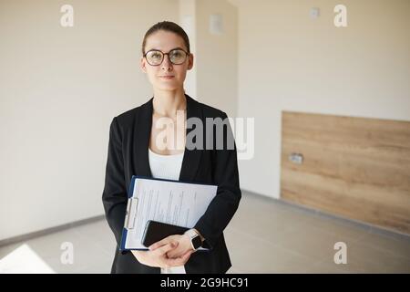 Waist up portrait of female real estate agent smiling at camera while standing in empty house, copy space Stock Photo