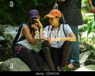 Amaga, Antioquia, Colombia - July 18 2021: Hispanic Women Sitting on Rocks on the Riverbank Taking Pictures in the Middle of Nature Stock Photo
