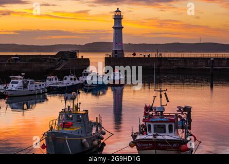 Small colourful fishing boats moored in Newhaven harbour at sunset with lighthouse, Edinburgh, Scotland, UK Stock Photo