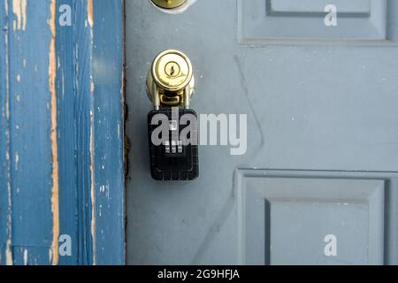 A closed combination lockbox padlock with letters on a worn door knob of a front door.