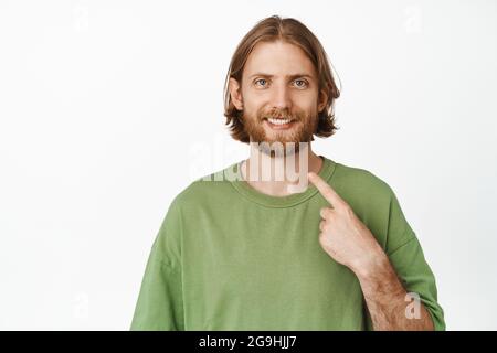 Its me. Happy handsome blond man pointing finger at himself, self-promoting, smiling pleased, volunteering, standing in green casual t-shirt over Stock Photo