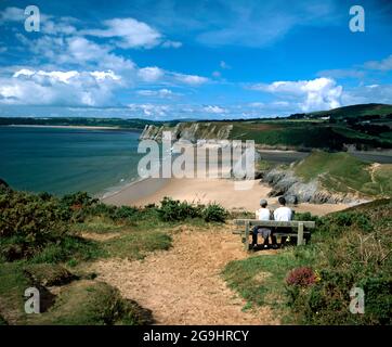 Couple sitting on a bench on Pennard Cliffs looking at the view of Three Cliffs Bay, Gower Peninsula, South Wales. Stock Photo