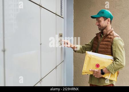 Side view portrait of smiling delivery man holding pizza and ringing doorbell, copy space Stock Photo