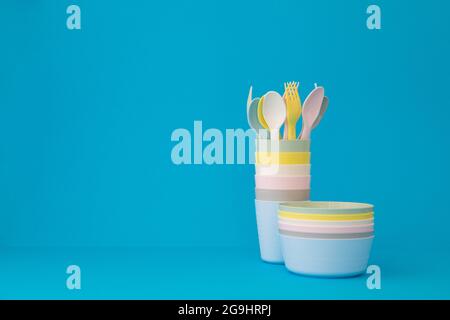 Colored reusable plates glasses spoons and forks on blue background copy space. Tableware for serving in pastel colors for a children's party Stock Photo