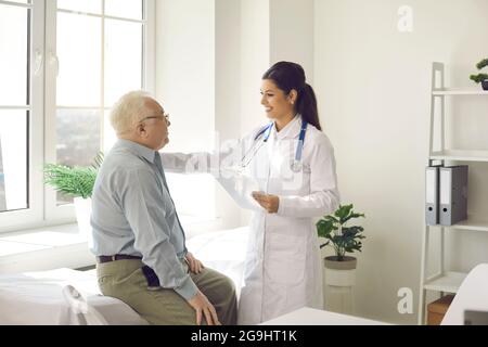 Woman doctor telling good treatment results to old patient at hospital office Stock Photo