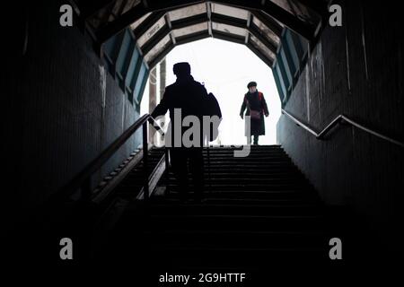 People go down the stairs. Silhouettes of people in the tunnel. Descending the subway in the city. Old people in Russia are walking along a pedestrian Stock Photo