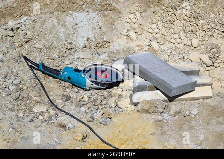 Electric tool with diamond disc for cutting stones lies on gravel. Angle grinder is ready for operation. Stone cutting technology. Close-up. Stock Photo