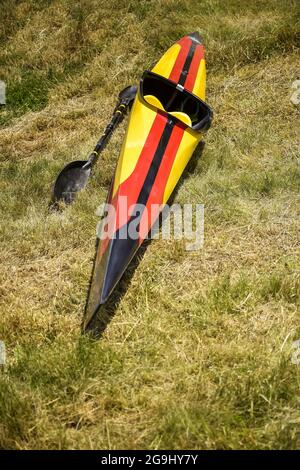 Single kayak, painted in colors of German flag, is drying on grass after competition. Paddle is lying next to it. Close-up. Selective focus. Stock Photo