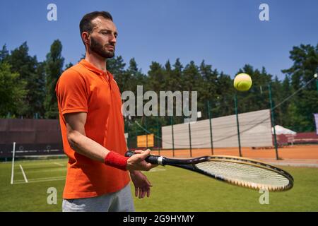 Concentrated mustached bearded athlete bouncing the ball on the racquet Stock Photo