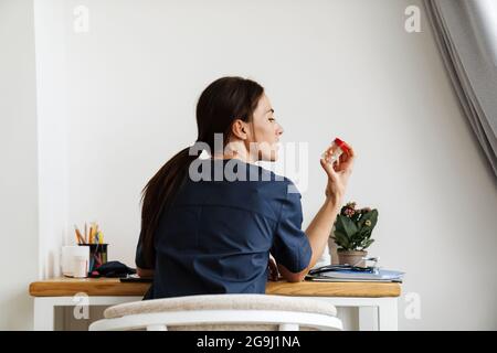 The back view of female doctor sitting at table looking sideways at jar of pills in room Stock Photo