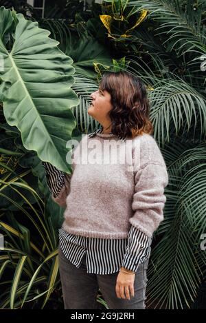 vertical image of woman looking sideways at an elephant ear leaf on a foliage Stock Photo