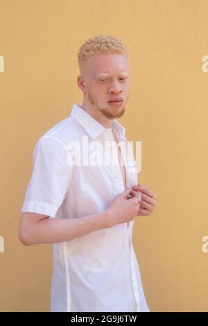 Germany, Cologne, Albino man in white shirt against yellow wall Stock Photo