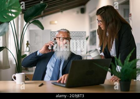 Senior businessman speaking on smartphone near colleague Stock Photo
