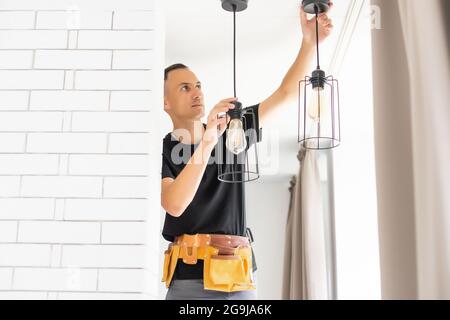 Worker repairing lamp on stretch ceiling indoors Stock Photo