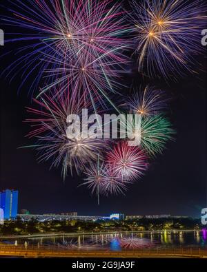 Festive colorful fireworks in the night sky over the city. Flashes and fireworks over the water of the city pond. Stock Photo