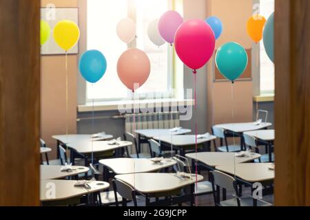 Entrance door of empty elementary primary school interior furniture children desk decorated with multicolored colorful air balloons against window Stock Photo