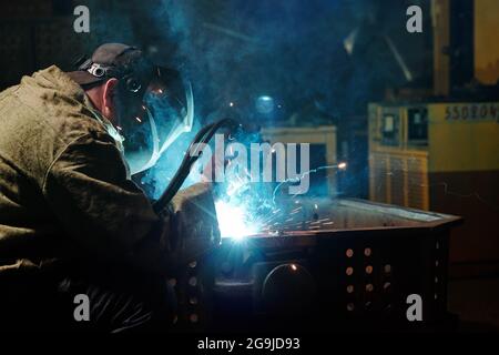 Worker in protective mask using angle grinder in workshop Stock Photo