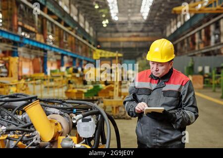 Two workers in helmets using tablet pc and discussing the work of machine equipment in the plant Stock Photo