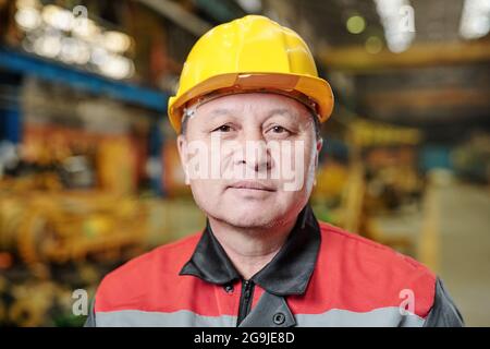 Mature foreman in helmet communicating on a wireless radio with his colleagues and using tablet pc in the plant Stock Photo