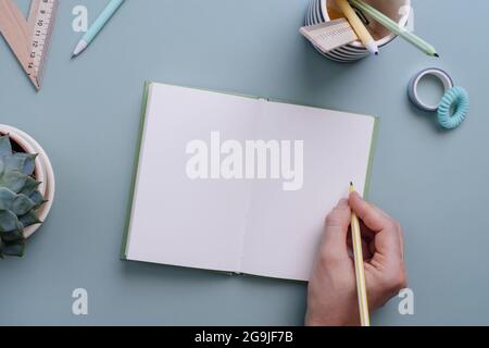 Women's hand ready to write in the empty notebook on the pastel blue background. Place for text. Working table for creative job, study or planning Stock Photo