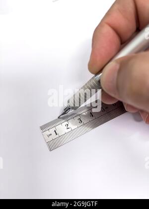 hand with a metal mechanical pencil making a straight line with a metallic millimeter ruler on a blank sheet of paper, selective focus in the ruler, v Stock Photo