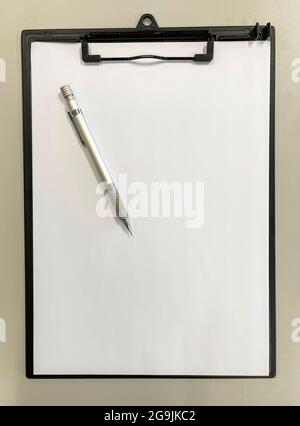 top view of a black clipboard folder with a blank sheet of paper and a metal mechanical pencil on a grey table, copy space, vertical Stock Photo